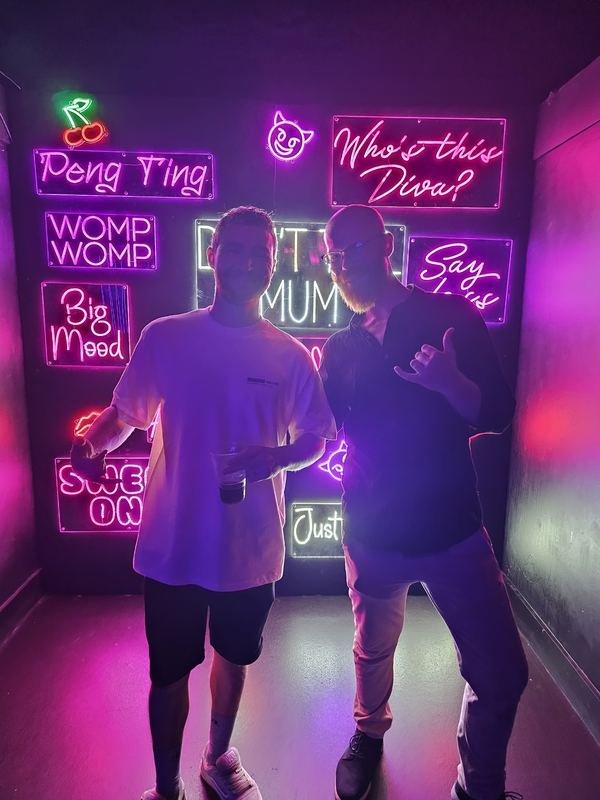 Dindalé and a friend posing in front of a wall of neon signs
